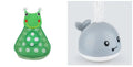 Whale-shaped electric bath toy spraying water with coloured LED lights, shown with base unit on blue background