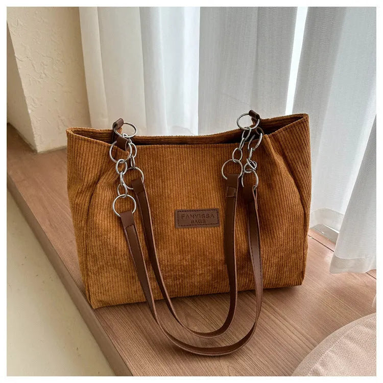 Corduroy one-shoulder tote handbag in black, showing three-dimensional pockets and a large main compartment.