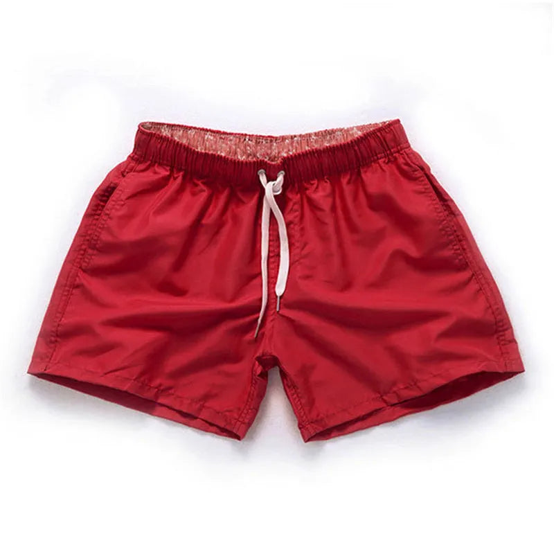 Men's plus size polyester surf shorts on a beach, showing straight leg fit in black and emerald green colours.