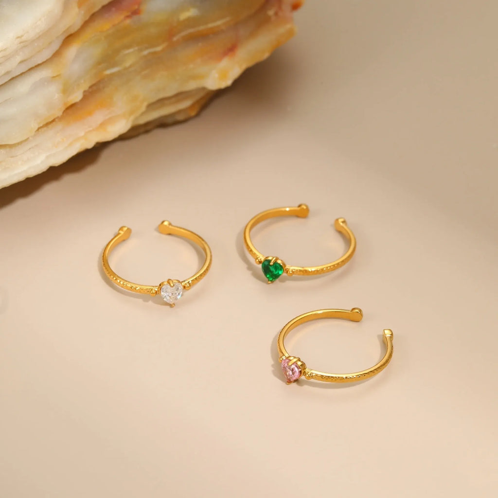 Open-ended adjustable ring with heart-shaped zircon decoration in geometric styling, shown in three colour variations.