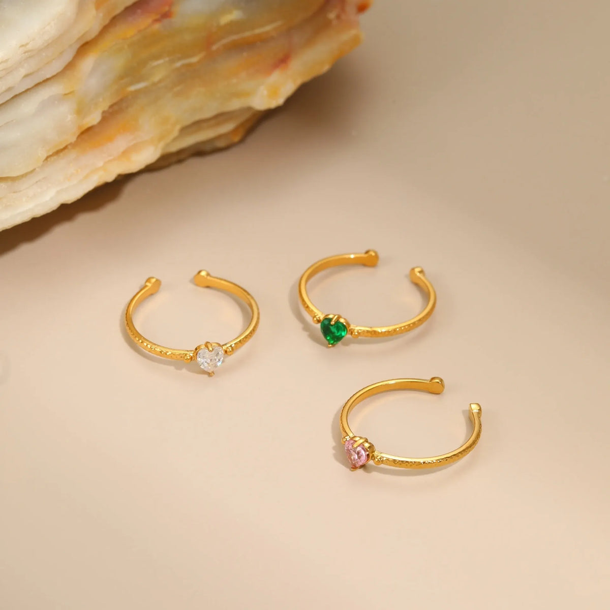 Open-ended adjustable ring with heart-shaped zircon decoration in geometric styling, shown in three colour variations.