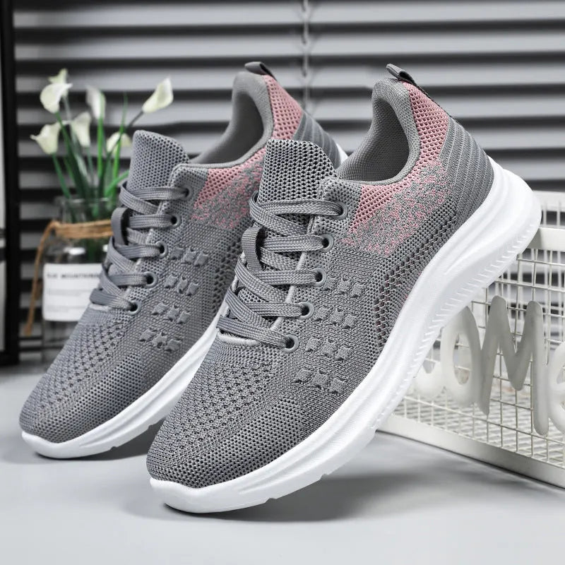 Women's low-top black mesh sneakers with white laces and a round toe on a grey background.