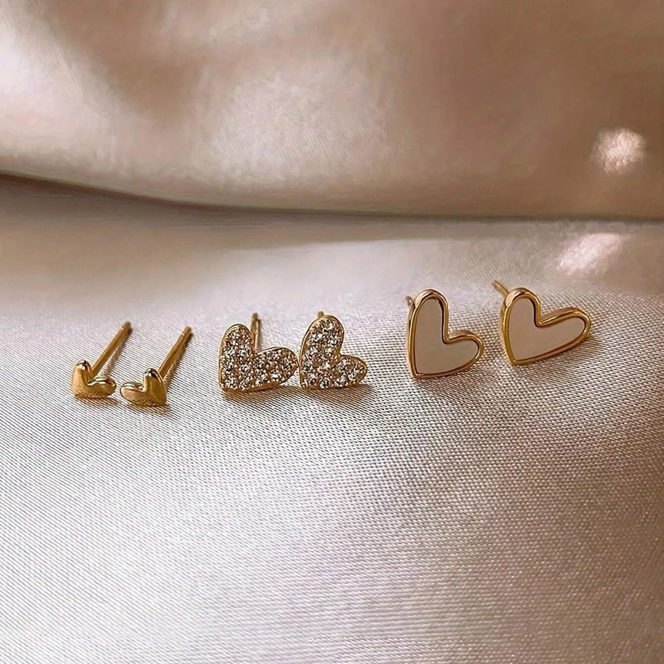 Three pairs of heart shape alloy earrings in gold, black, black white, and pink colours with love design elements