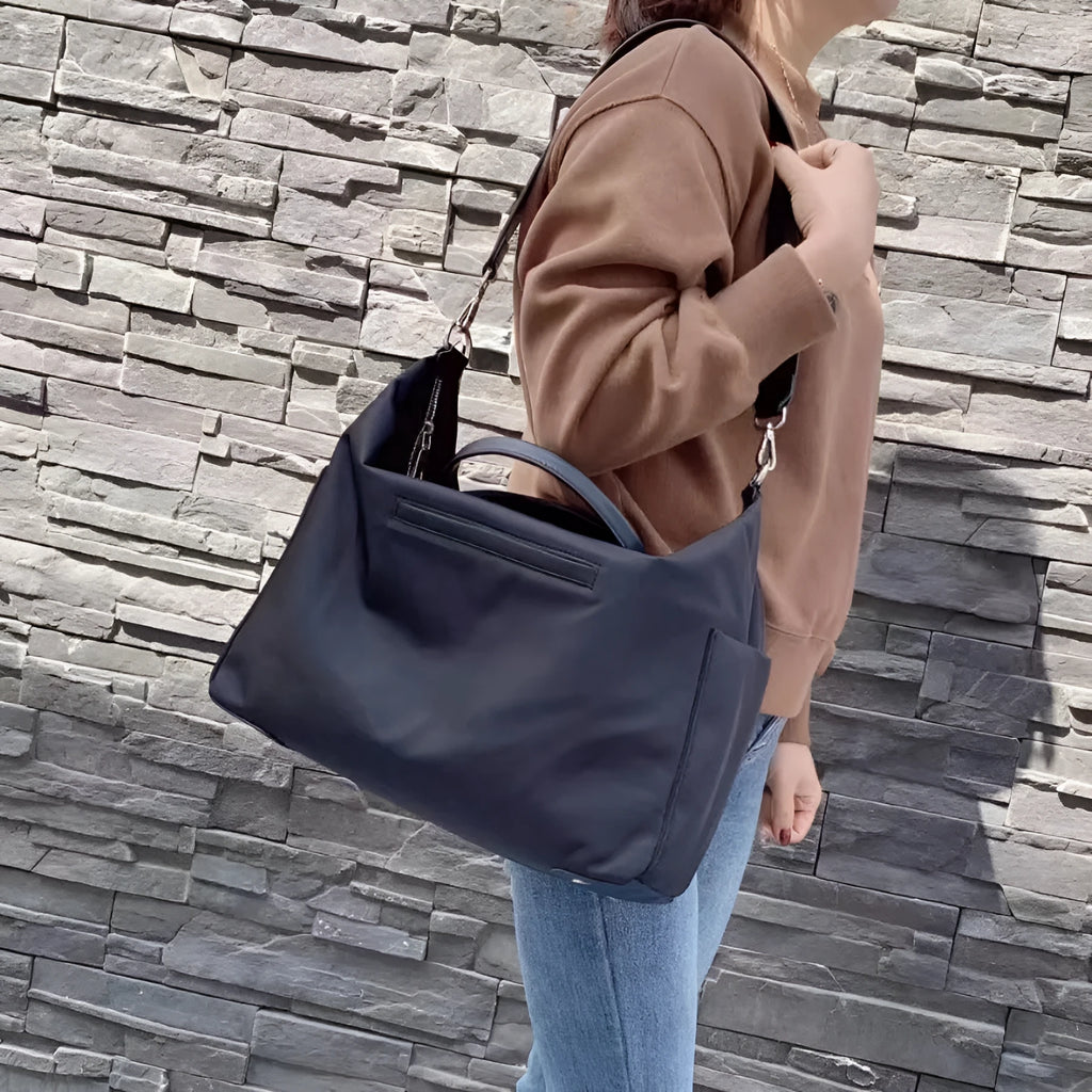 Black nylon waterproof shoulder bag with leather handbag detail and large main compartment.