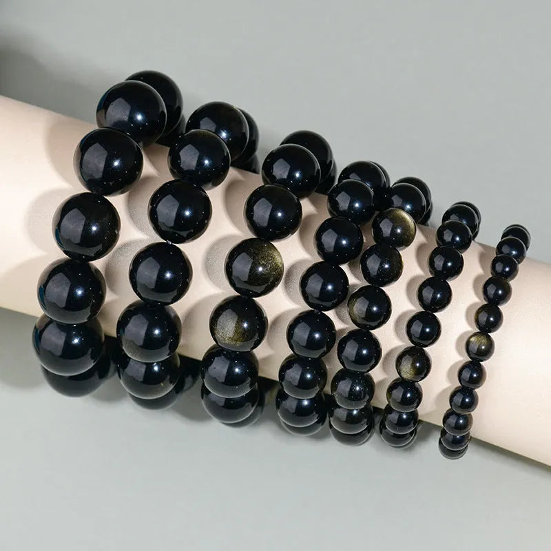 Hand-woven round obsidian bracelet in black stone, shown on a wrist.
