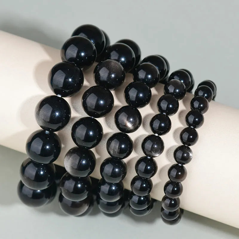 Hand-woven round obsidian bracelet in black stone, shown on a wrist.