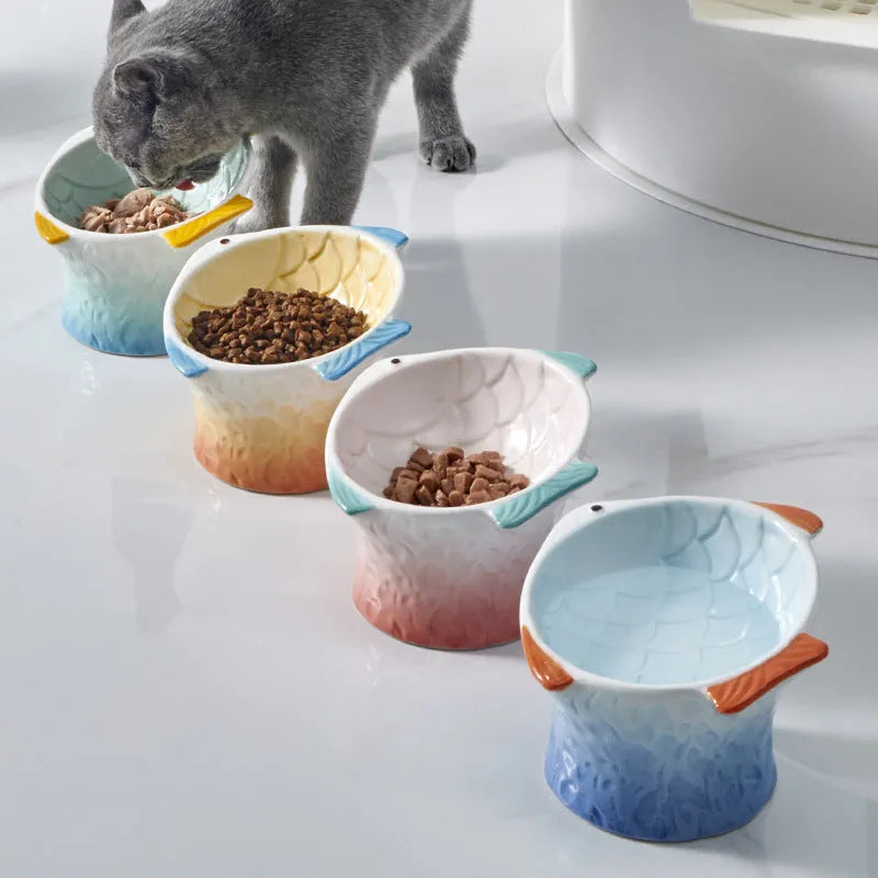 Four coloured fish-shaped ceramic cat bowls with tilted bases on a table.