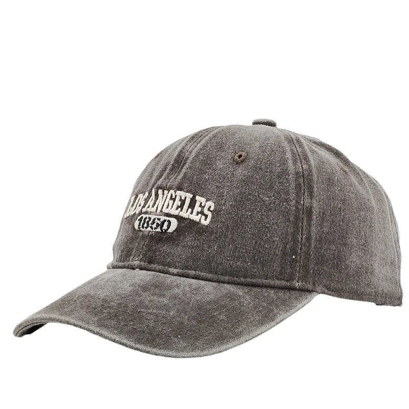 Retro style peaked cap with embroidered distressed letters on the front, shown in beige colour.