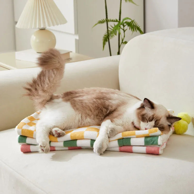 Green plaid plush fleece pet blanket with fur ball trim, laid flat as a dog bed or cat mat.