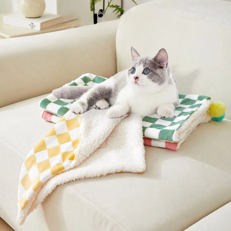 Green plaid plush fleece pet blanket with fur ball trim, laid flat as a dog bed or cat mat.
