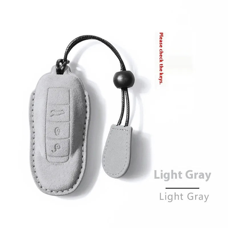 Suede car key cover shown in cement grey, dark green, light grey, and orange colour options.