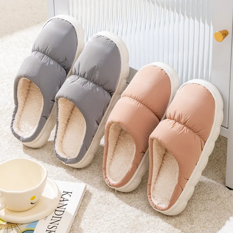 Pair of grey artificial leather slippers with a thick rubber sole and plush lining, shown on a wooden floor.
