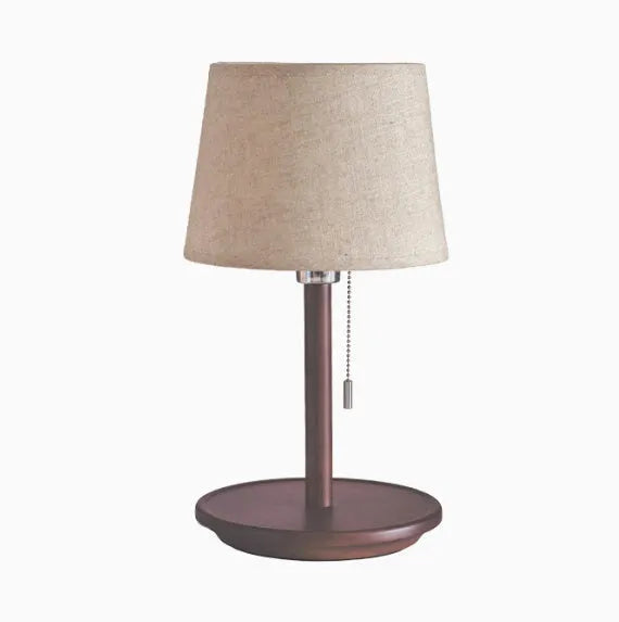 Walnut coloured solid wood bedside lamp with fabric shade on wooden surface