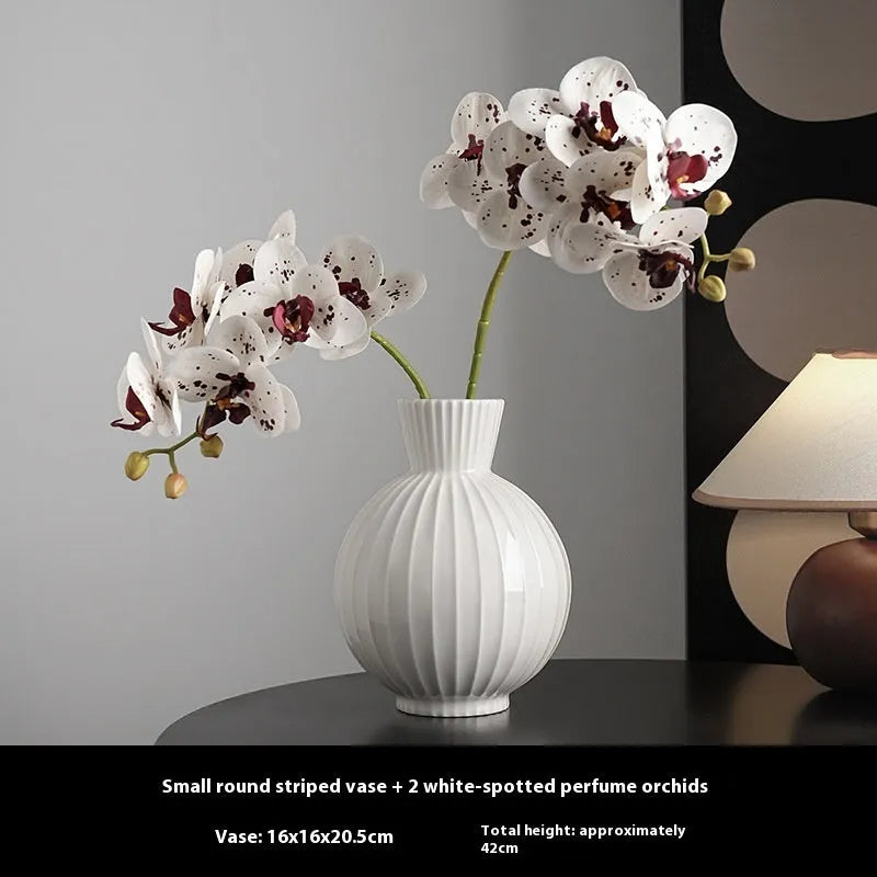 White ceramic ball vase with blue stripes and artificial orchid stems on wooden table.