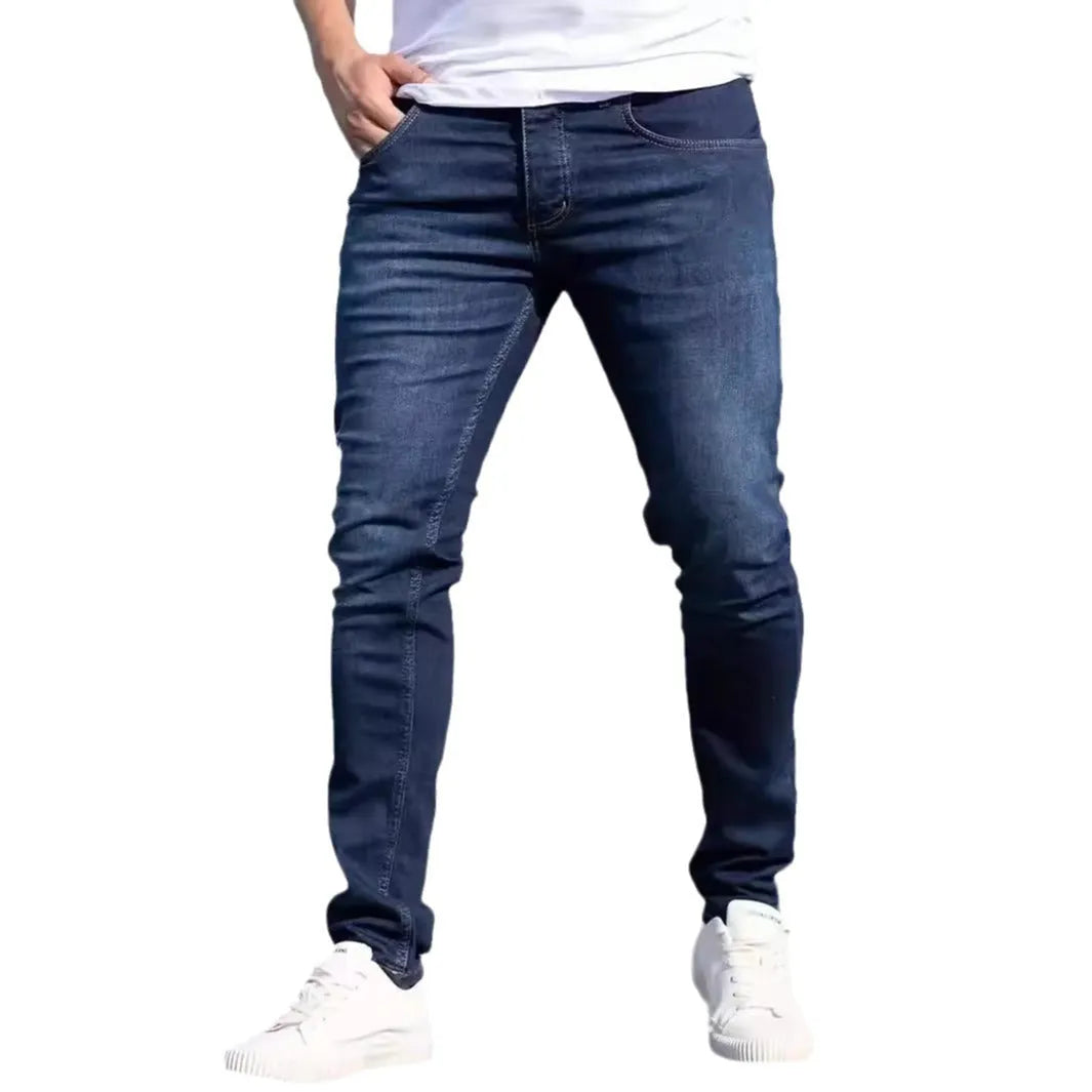 Man wearing dark blue slim-fit skinny jeans with a zipper fly, showcasing the mid-waist and street fashion style.