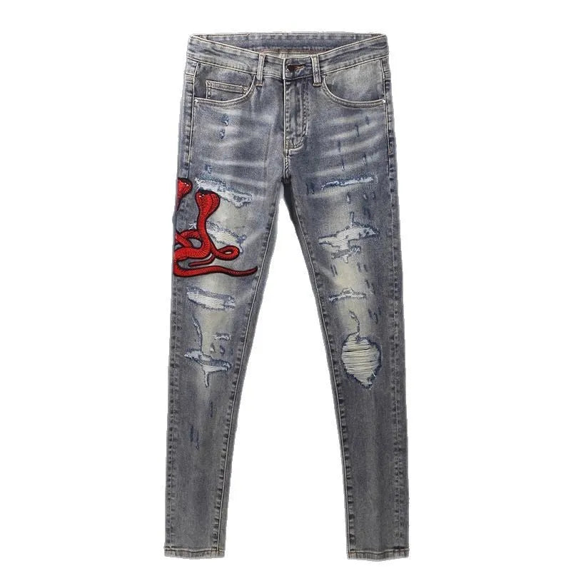 Men's blue slim fit jeans with distressed holes and embroidered patches on faded denim.