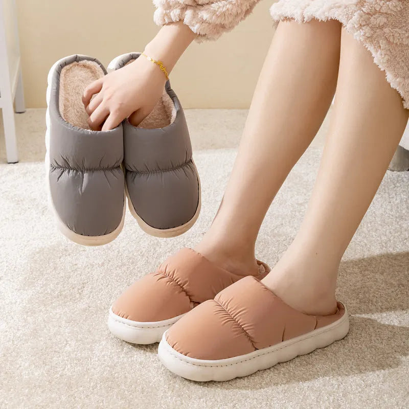 Pair of grey artificial leather slippers with a thick rubber sole and plush lining, shown on a wooden floor.