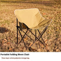 Beige folding camping chair with reclined back and steel frame on grass.