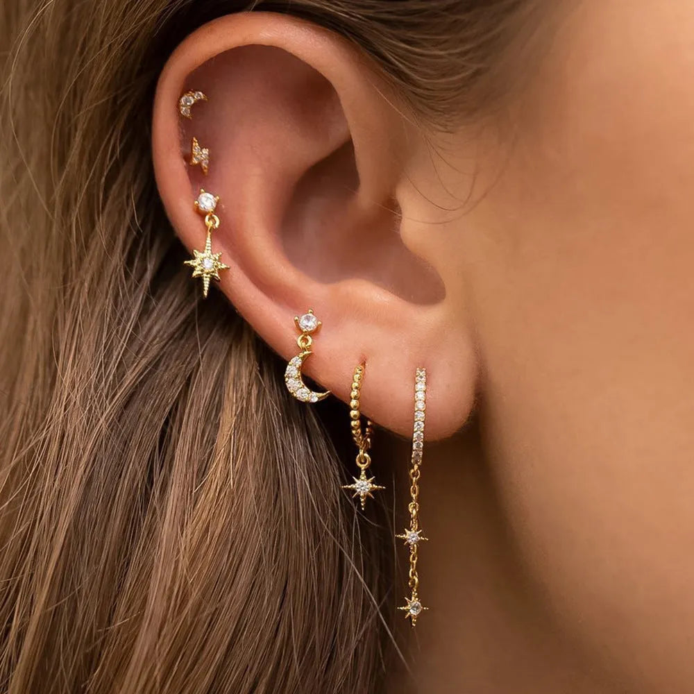 Set of six gold chain tassel drop earrings with crystal studs on a white background.