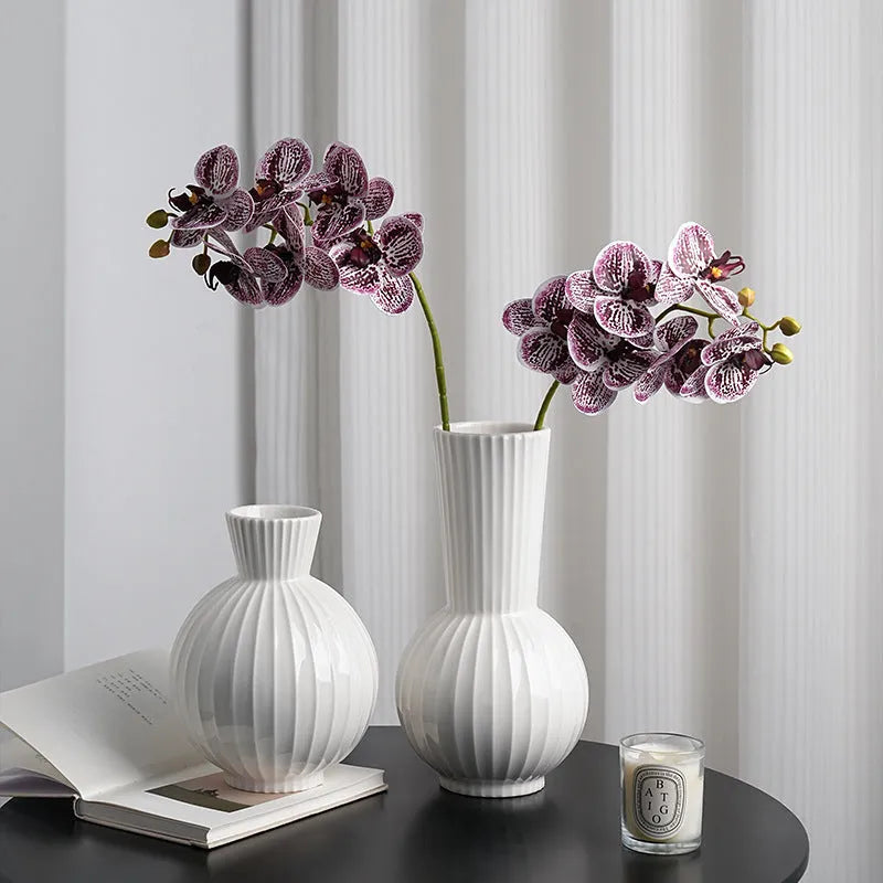 White ceramic ball vase with blue stripes and artificial orchid stems on wooden table.
