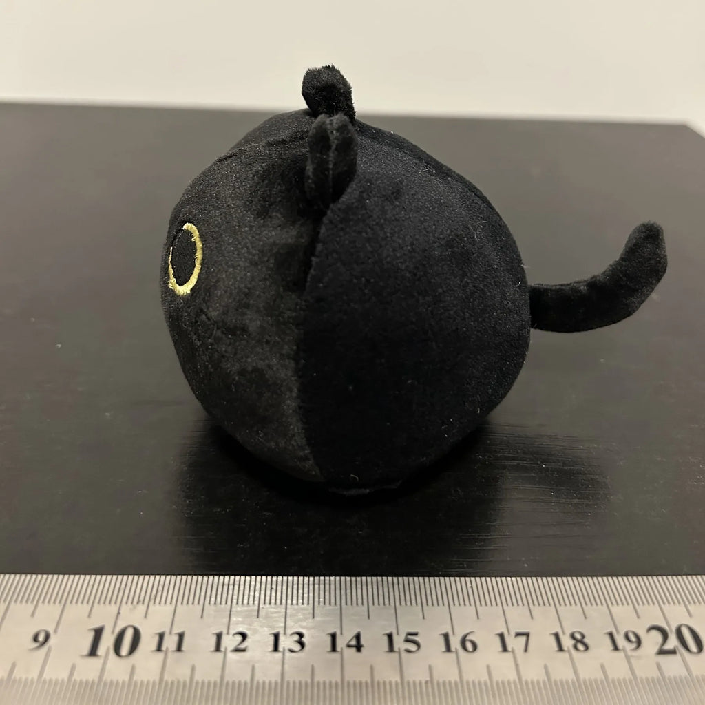 Fluffy black cat plush toy used as a soft pillow cushion on a sofa.