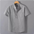 A man's casual beige slub linen shirt with a stand collar and short sleeves, laid flat to show its loose fit.