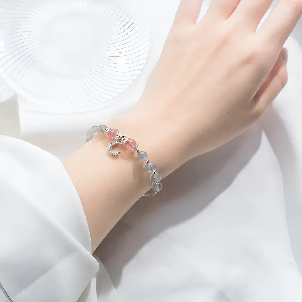 Handmade adjustable moonstone bracelet with a silver crescent moon charm and clear crystal accent on a grey background.