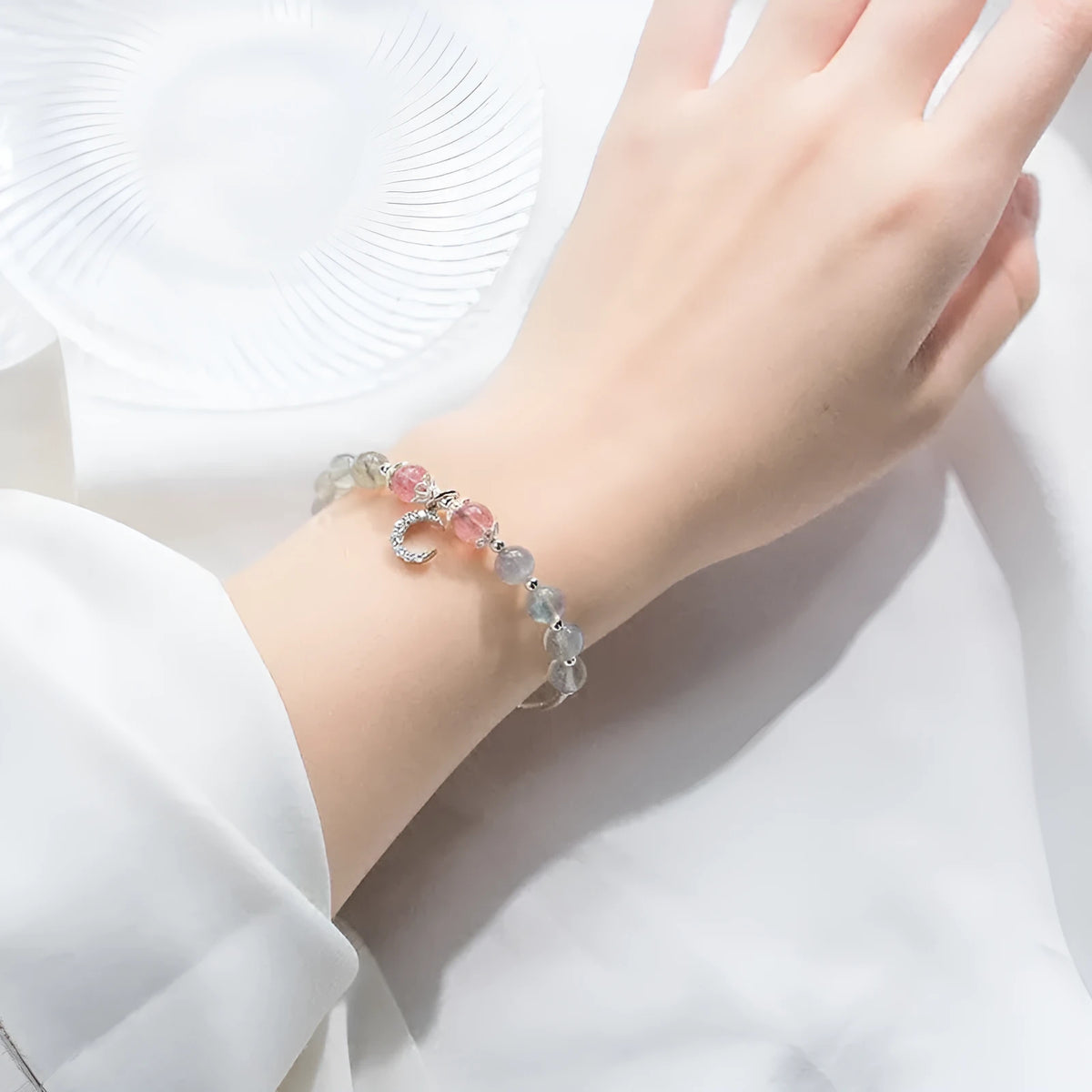 Handmade adjustable moonstone bracelet with a silver crescent moon charm and clear crystal accent on a grey background.