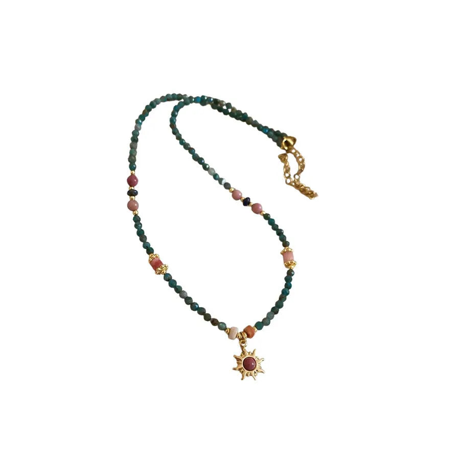 Stone sun pendant freshwater pearl necklace with gold blue pink chain on display.