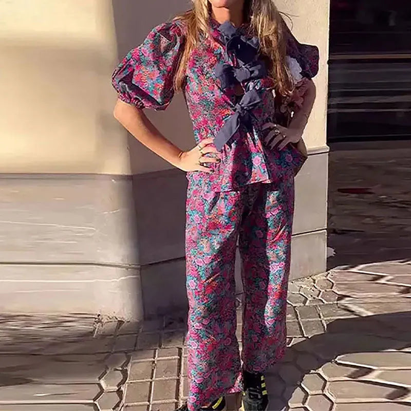 Women's floral print trouser suit set featuring a tie-neck blouse with puff sleeves and matching trousers.