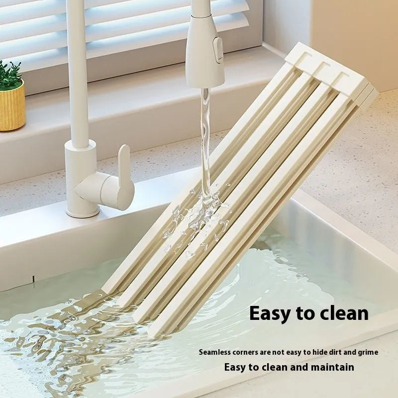 Milky white foldable stainless steel kitchen draining rack shown unfolded next to a sink.