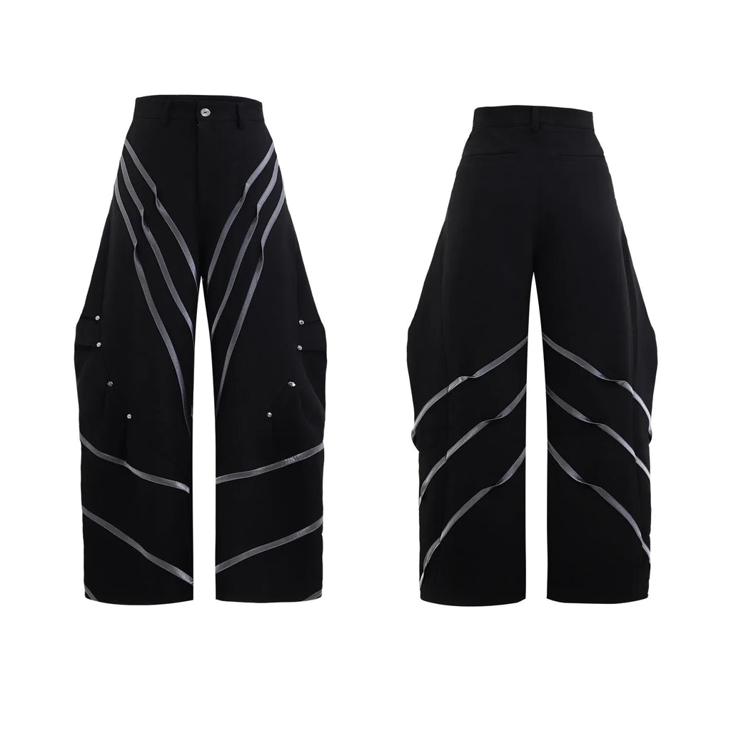 Men's black trousers with structured three-dimensional cut and metal rivet pleats on the legs.