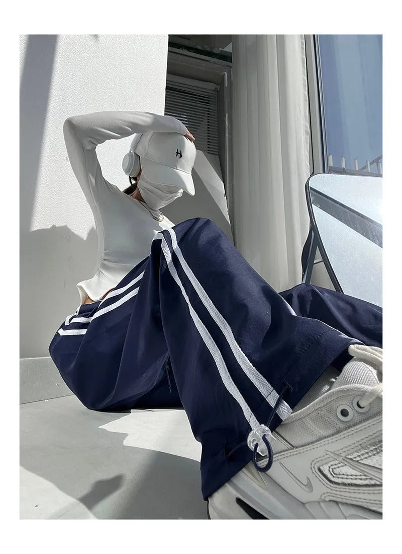Women's navy blue loose straight-leg trousers with white contrast ribbon detail on parallel bars, low waist, draping silhouette