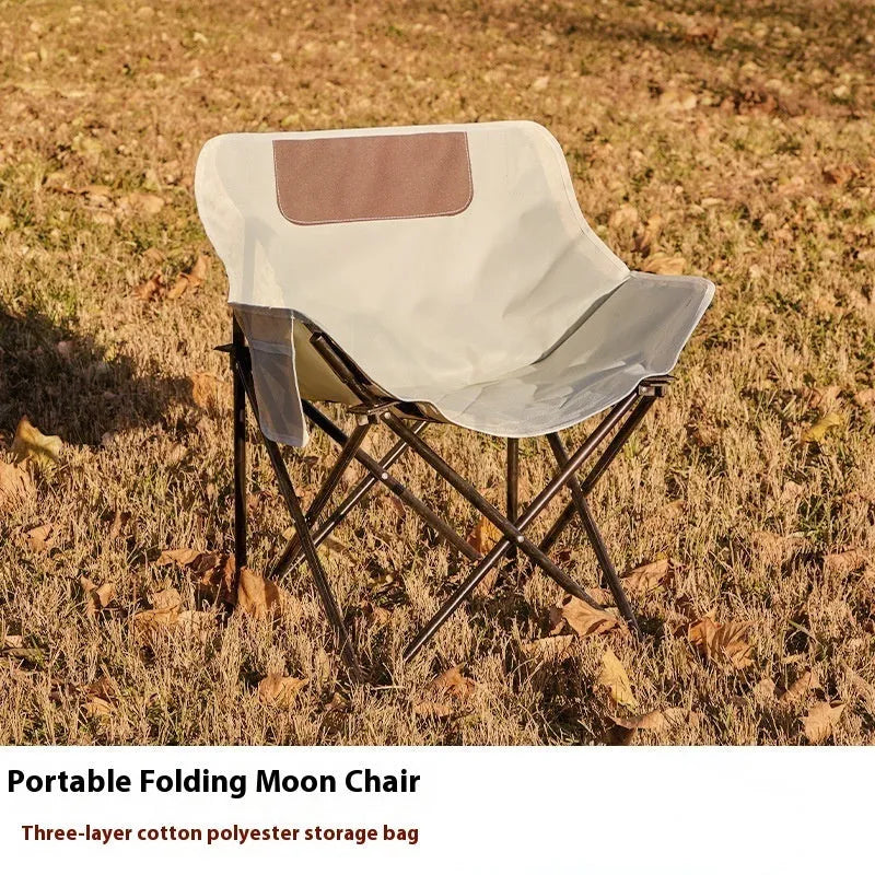 Beige folding camping chair with reclined back and steel frame on grass.