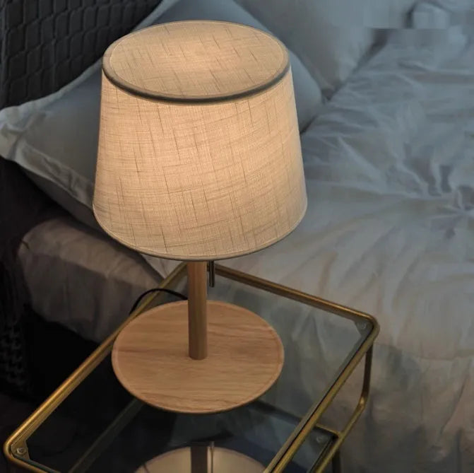 Walnut coloured solid wood bedside lamp with fabric shade on wooden surface
