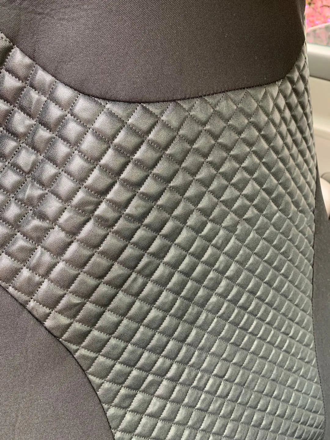 Black quilted car seat cover made of PU and polyester fabric with plastic hooks.
