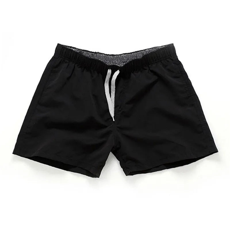 Men's plus size polyester surf shorts on a beach, showing straight leg fit in black and emerald green colours.