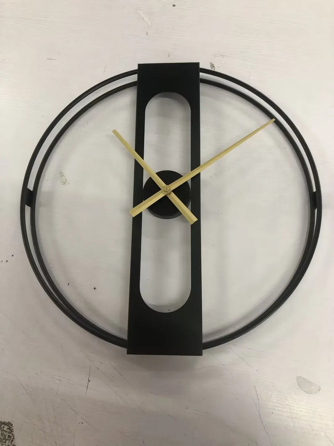 A large 50 cm round metal wall clock on a wall, available in black or gold finish.