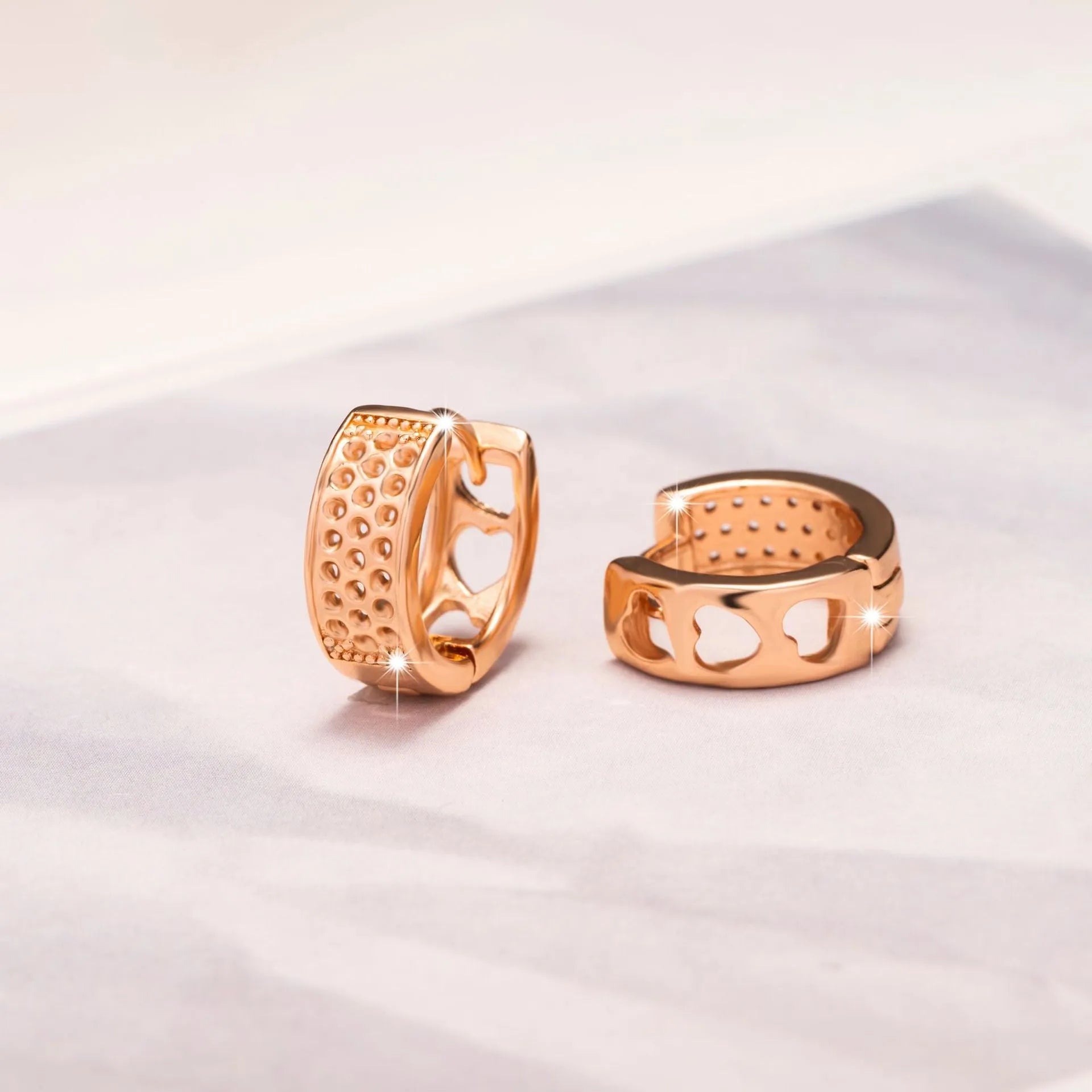 Rose gold coloured circular earrings with a hollowed-out three-heart design.