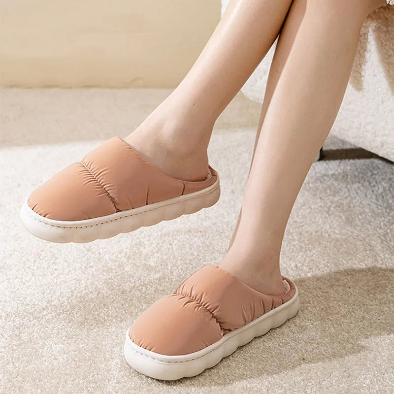 Pair of grey artificial leather slippers with a thick rubber sole and plush lining, shown on a wooden floor.
