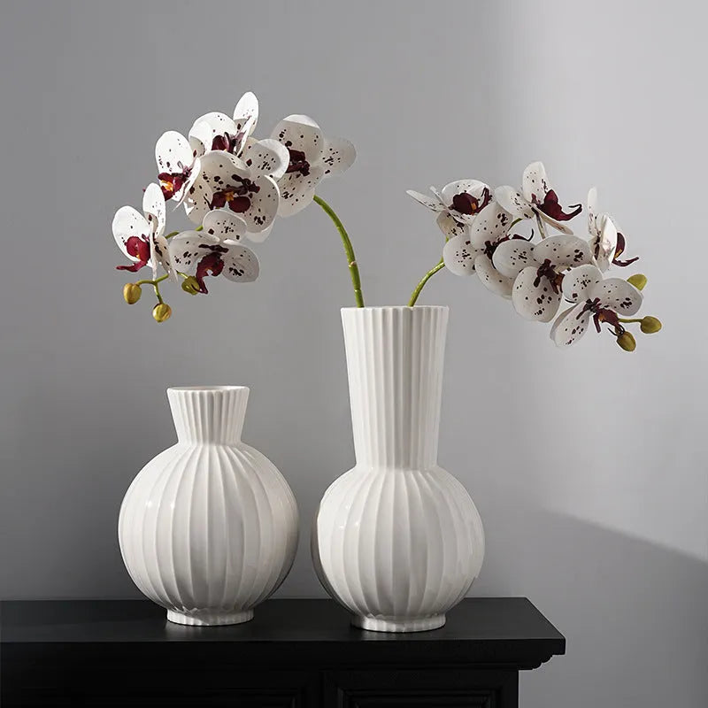 White ceramic ball vase with blue stripes and artificial orchid stems on wooden table.