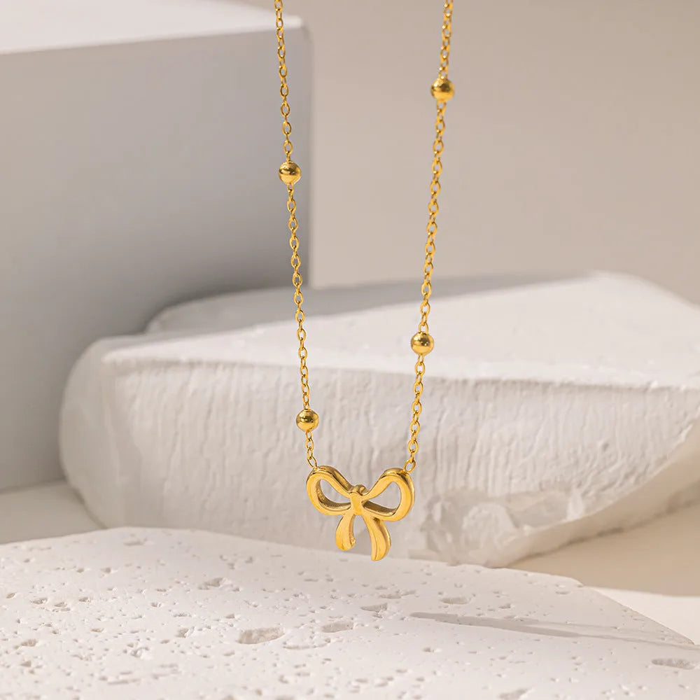 Gold titanium steel bow necklace on a cross chain, adjustable between 41cm and 50cm.