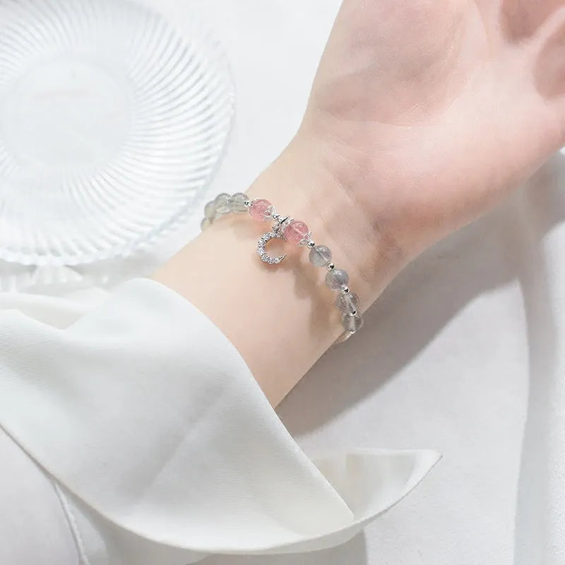 Handmade adjustable moonstone bracelet with a silver crescent moon charm and clear crystal accent on a grey background.