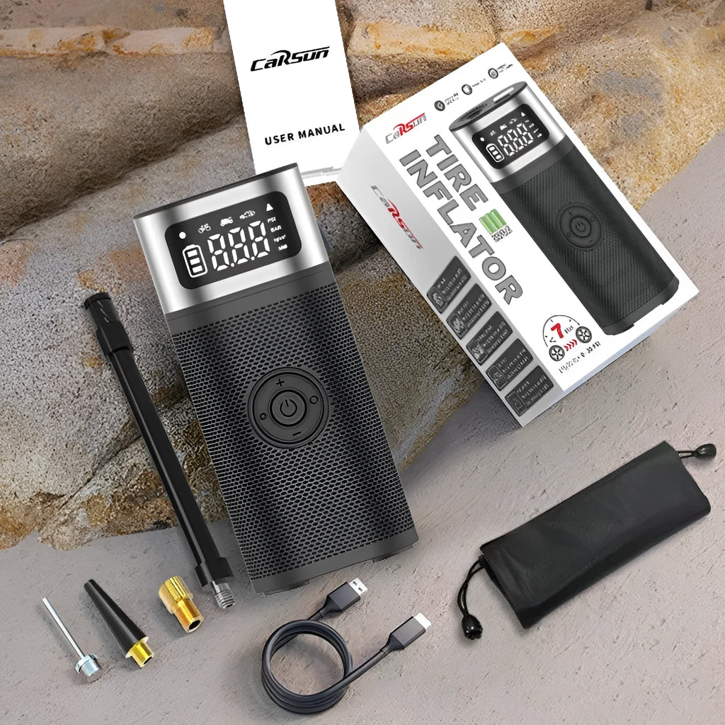Black portable wireless air pump with digital display, LED light, and attached inflation tube on a textured surface.