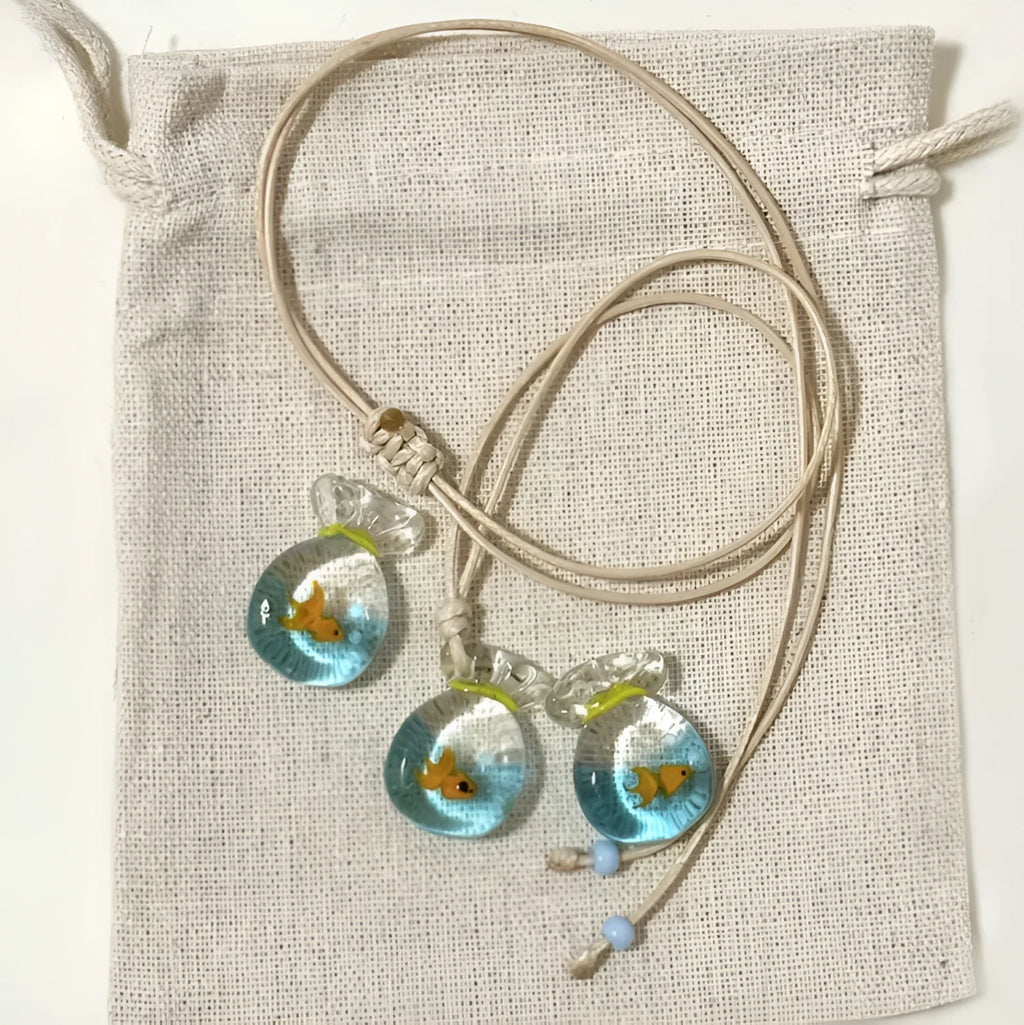 Women's necklace with small coloured glaze fish lucky bag pendant on a braided cotton and linen chain.