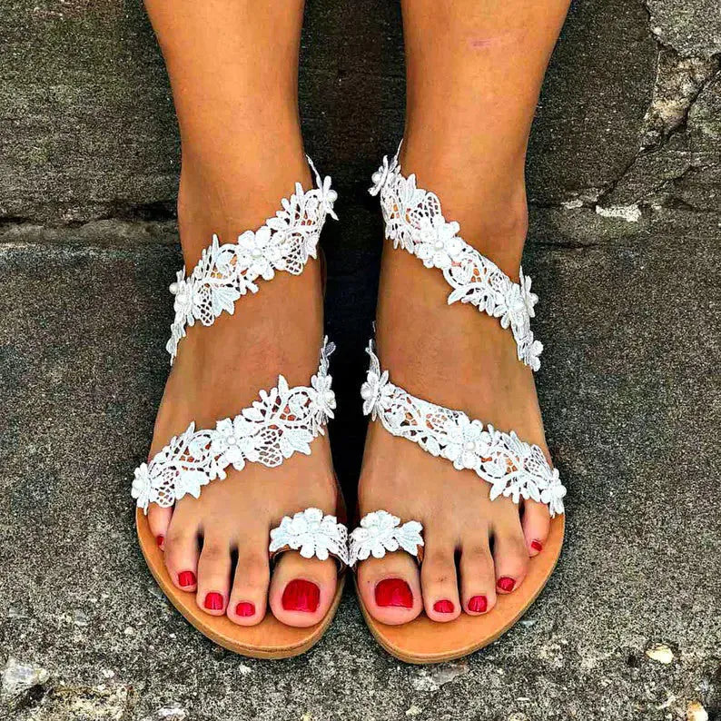 White women's flat sandals with rhinestone flower decoration on patent leather upper, showing round toe and slip-on design