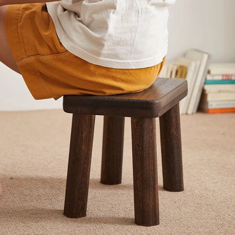 Solid wood changing stool with distressed finish and bracket legs in a living room setting.