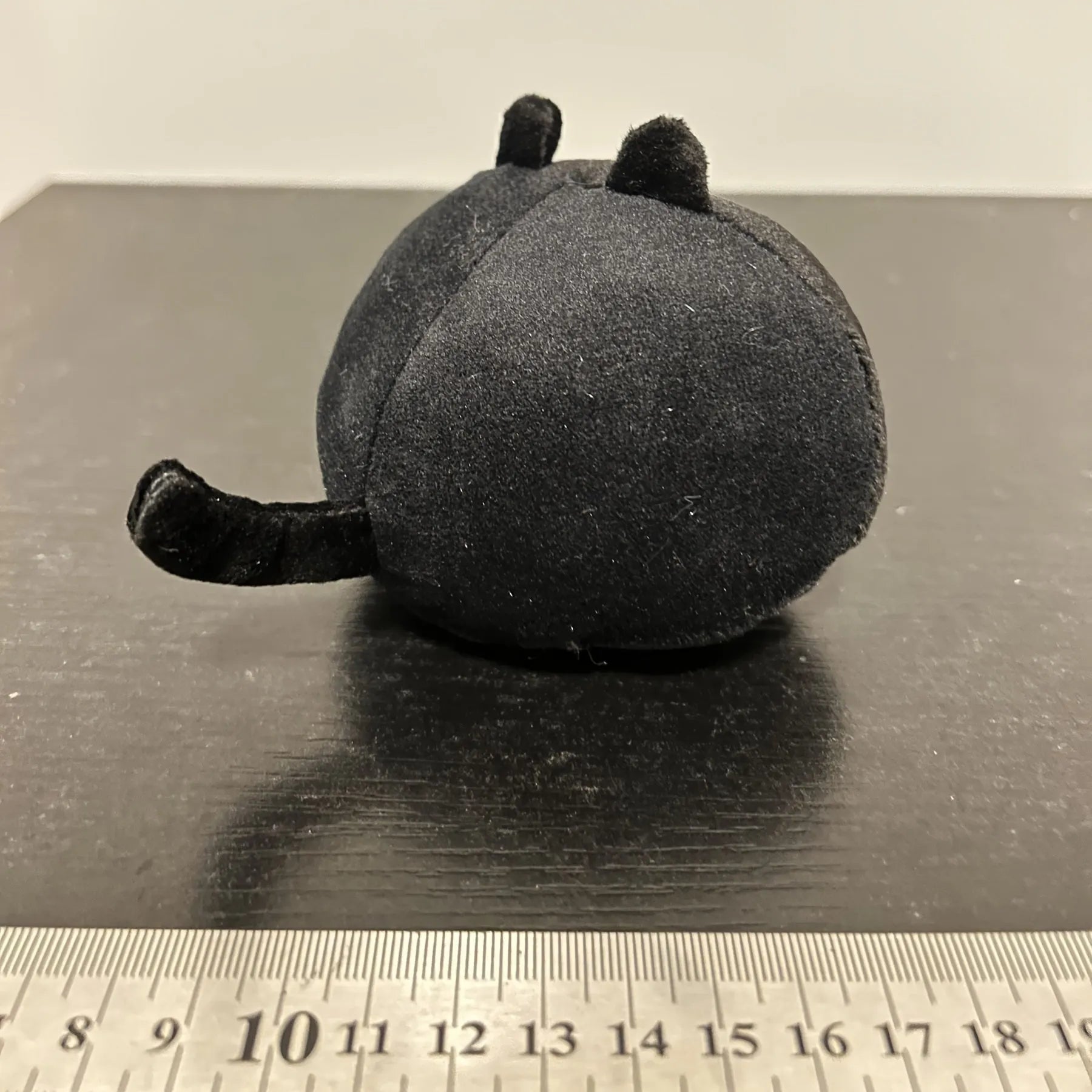 Fluffy black cat plush toy used as a soft pillow cushion on a sofa.