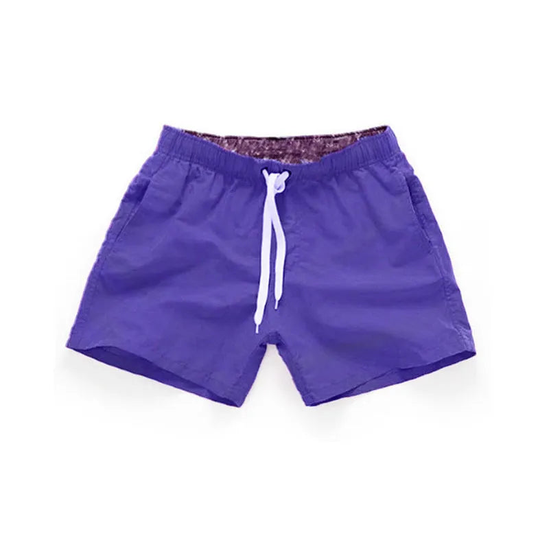 Men's plus size polyester surf shorts on a beach, showing straight leg fit in black and emerald green colours.