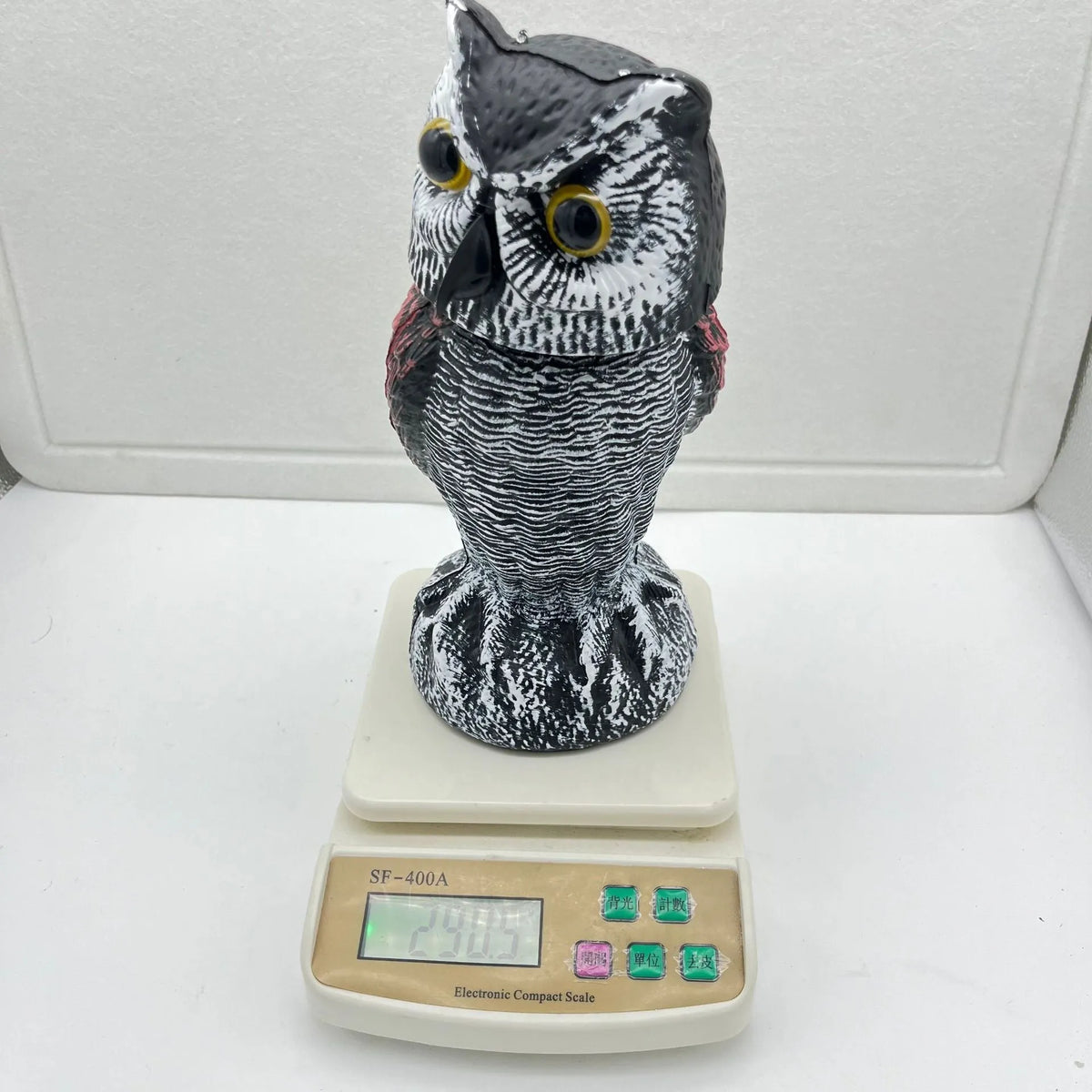 Polyethylene artificial owl bird scarer ornament with moving head, shown in a garden setting.